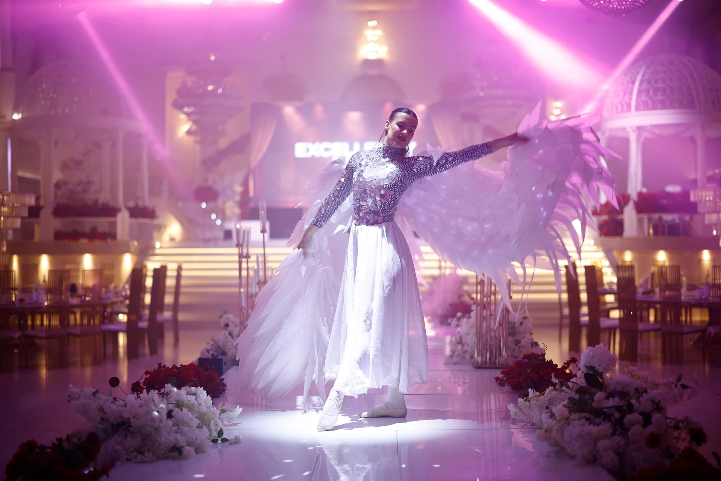Dancer with illuminated white wings under purple stage lights