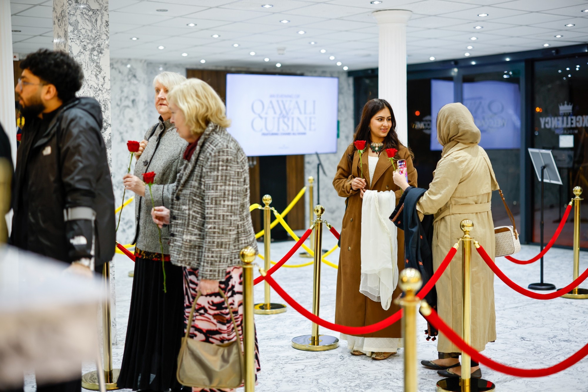 Guests arriving for An Evening of Qawali & Cuisine, holding red roses behind a red rope barrier
