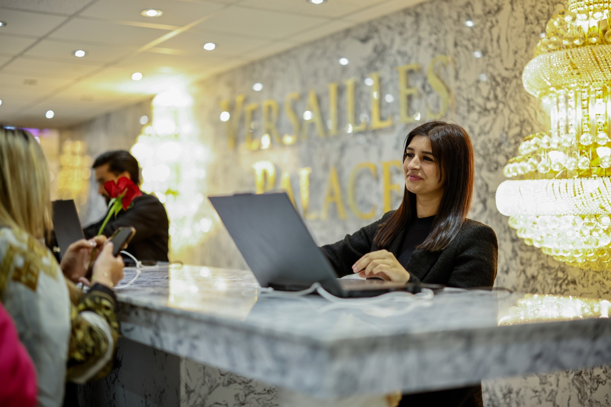 A guest being checked in at the marble Versailles Palace reception desk beneath a gold chandelier